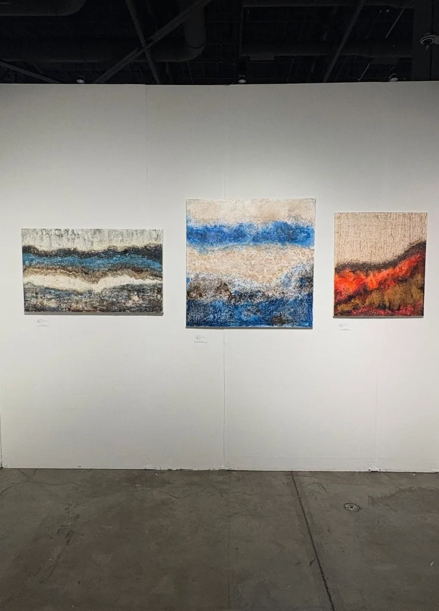 Three paintings by Marina Elizalde on a wall at the Seattle Art Fair